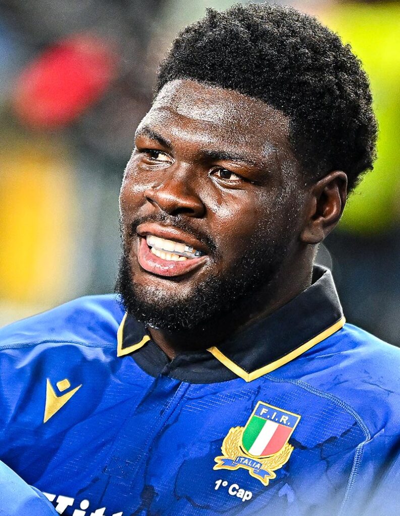 Enoch Opoku-Gyamfi wearing a blue Italy rugby kit with "1st cap" underneath the national badge.