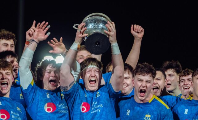 Captain Max Pearce lifts the BUCS Super Rugby league champions trophy as his University of Bath men's 1st XV team-mates celebrate around him