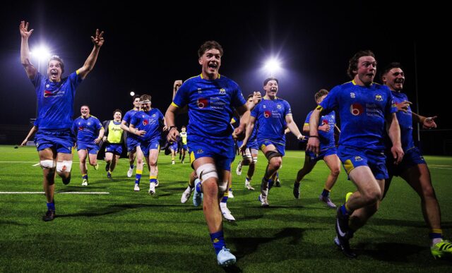 University of Bath Rugby Club players, wearing blue, run towards the camera in celebration after a crucial win against Loughborough
