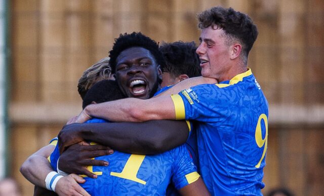 Rugby players wearing blue kit hugging in celebration.
