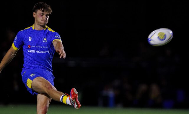 A rugby player wearing kicking a ball, which is flying through the air