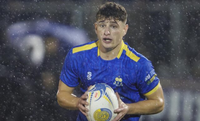 A rugby player, wearing blue, holding a rugby ball during a match